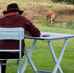 Une personne se tient assise de dos et écrit sur une table dans un jardin.