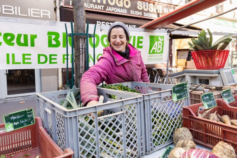 Une femme tient un stand de légumes bio au marché