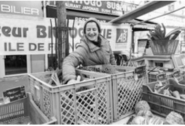 Une femme tient un stand de légumes bio au marché