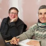 Deux femmes travaillent devant un écran et sourient au photographe