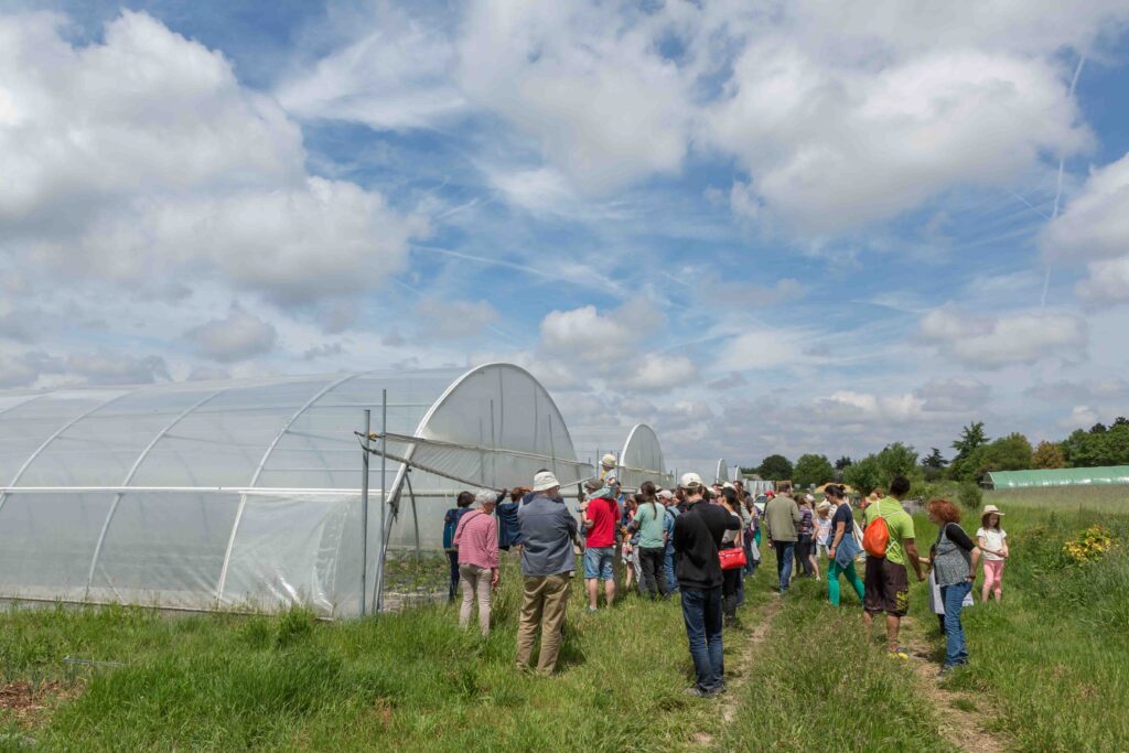 De nombreuses personnes visitent une ferme et se tiennent devant l'entrée de deux grands tunnels