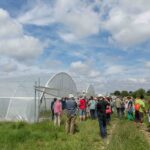 De nombreuses personnes visitent une ferme et se tiennent devant l'entrée de deux grands tunnels