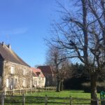 Vue d'un bâtiment ancien, devant lequel on devine des jeux pour enfants et de grands arbres