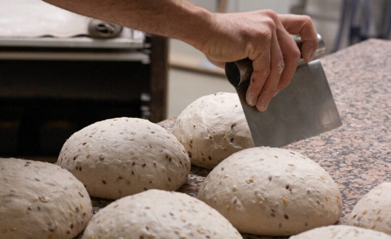 Des pains prêts à être passés au four recoivent une marque de la main d'un boulanger, à l'aide d'un outil.