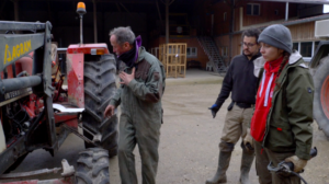 Devant une ferme, un formateur et deux stagiaires se tiennent devant un tracteur pour une formation sur le graissage d'engins