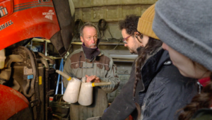 Un formateur présente les outils pour effectuer les mises à niveau et vidange de tracteur devant trois personnes en formation.