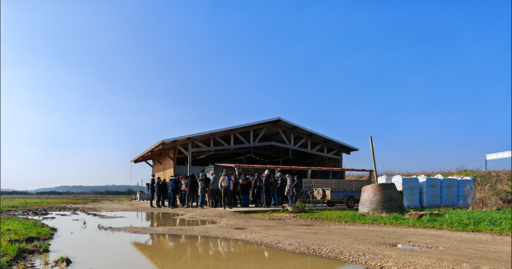 Un groupe de personnes se tient devant un bâtiment agricole en extérieur