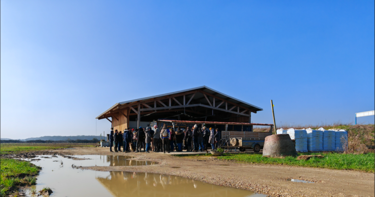 Un groupe de personnes se tient devant un bâtiment agricole en extérieur