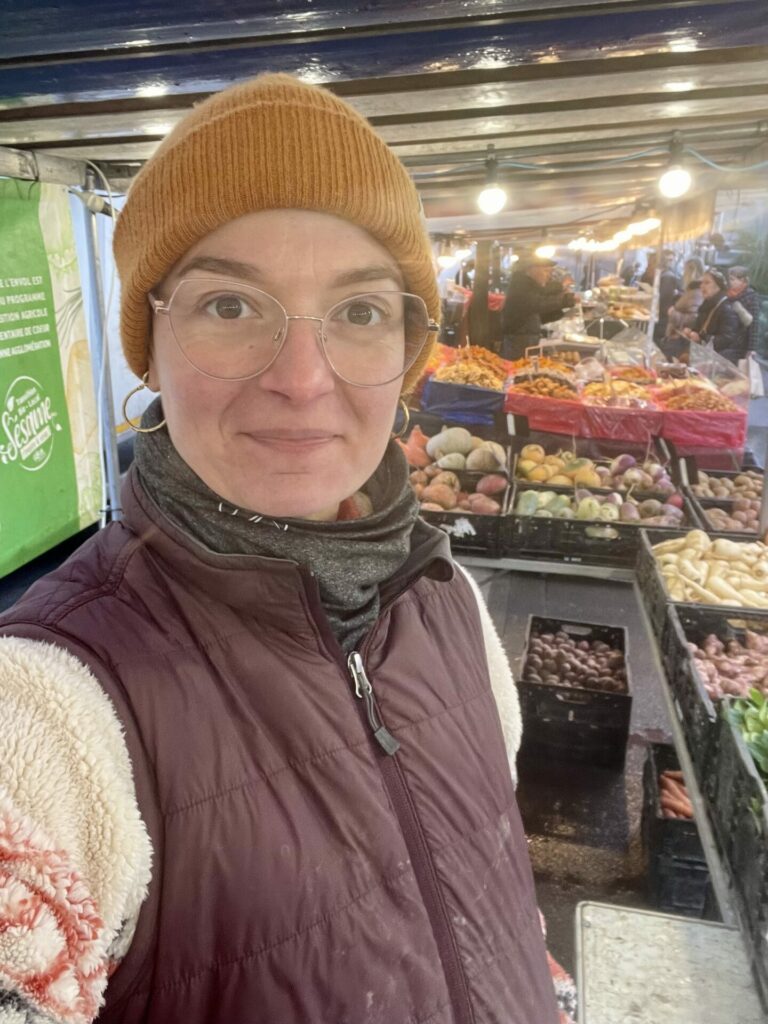 Une femme pose en photo devant un étal de légumes