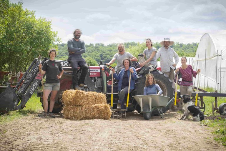 Une dizaine de personnes posent avec leurs outils et des bottes de foin à côté de serres maraîchères